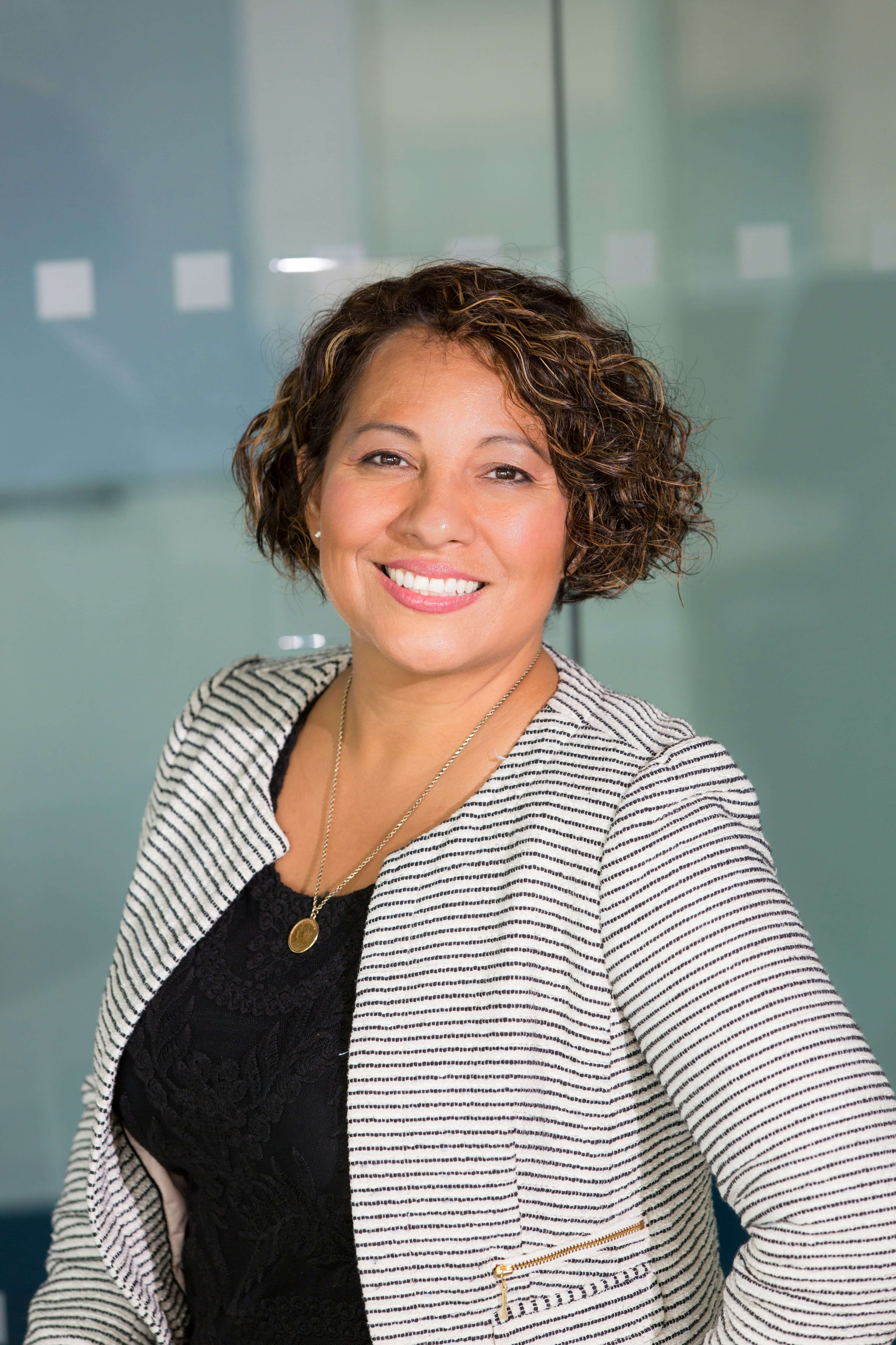 Smiling woman in office attire standing in a bright room.